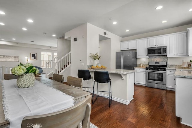 kitchen featuring dark wood-type flooring, light stone counters, appliances with stainless steel finishes, a peninsula, and white cabinets