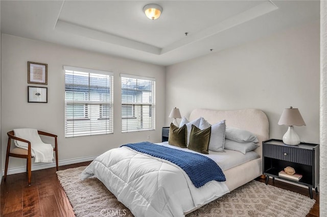 bedroom featuring a tray ceiling, baseboards, and wood finished floors