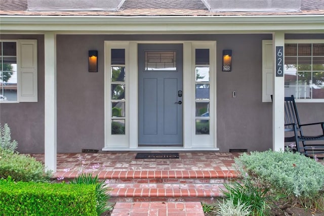 entrance to property featuring stucco siding, a porch, and a shingled roof