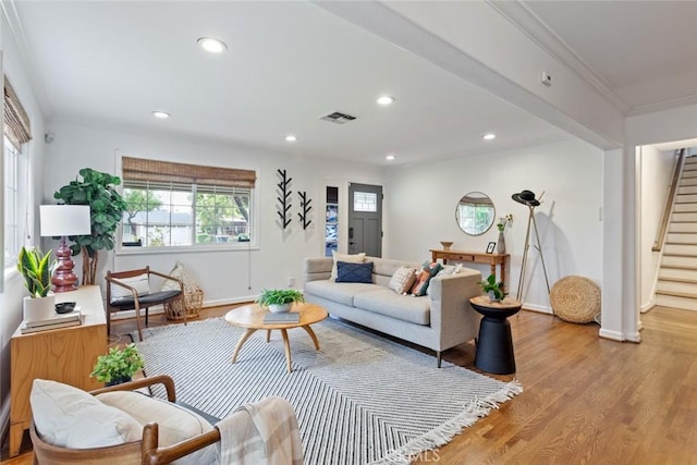 living room with stairway, light wood-style flooring, visible vents, and ornamental molding