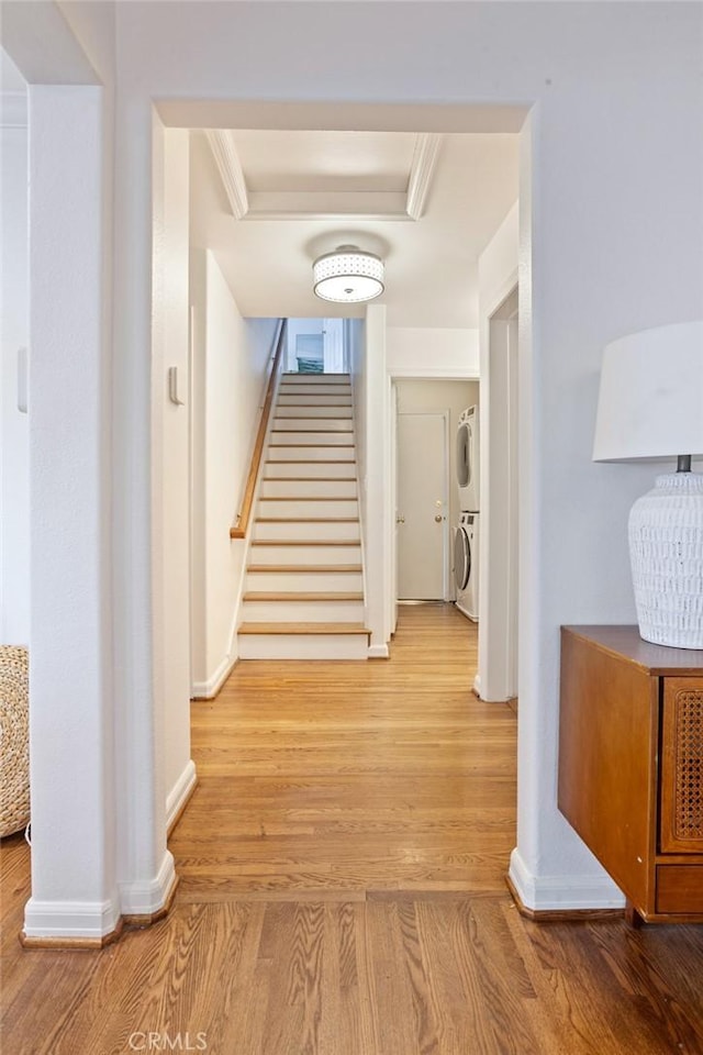 hallway with stairway, stacked washing maching and dryer, baseboards, and wood finished floors