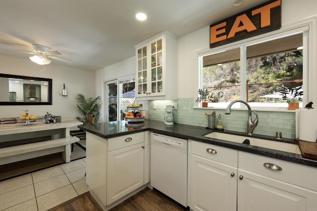 kitchen with tasteful backsplash, a peninsula, white dishwasher, white cabinets, and a sink