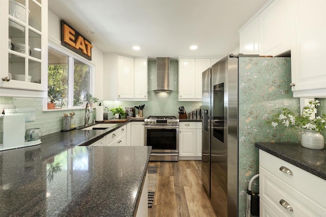 kitchen featuring a sink, wall chimney range hood, white cabinets, stainless steel appliances, and dark wood-style flooring