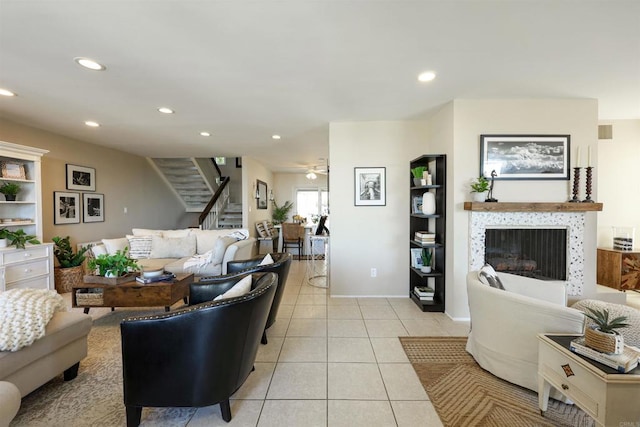 living room featuring a tiled fireplace, stairs, light tile patterned floors, recessed lighting, and a ceiling fan