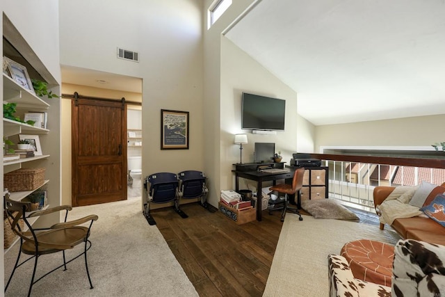 living room with a high ceiling, a barn door, dark wood-type flooring, and visible vents