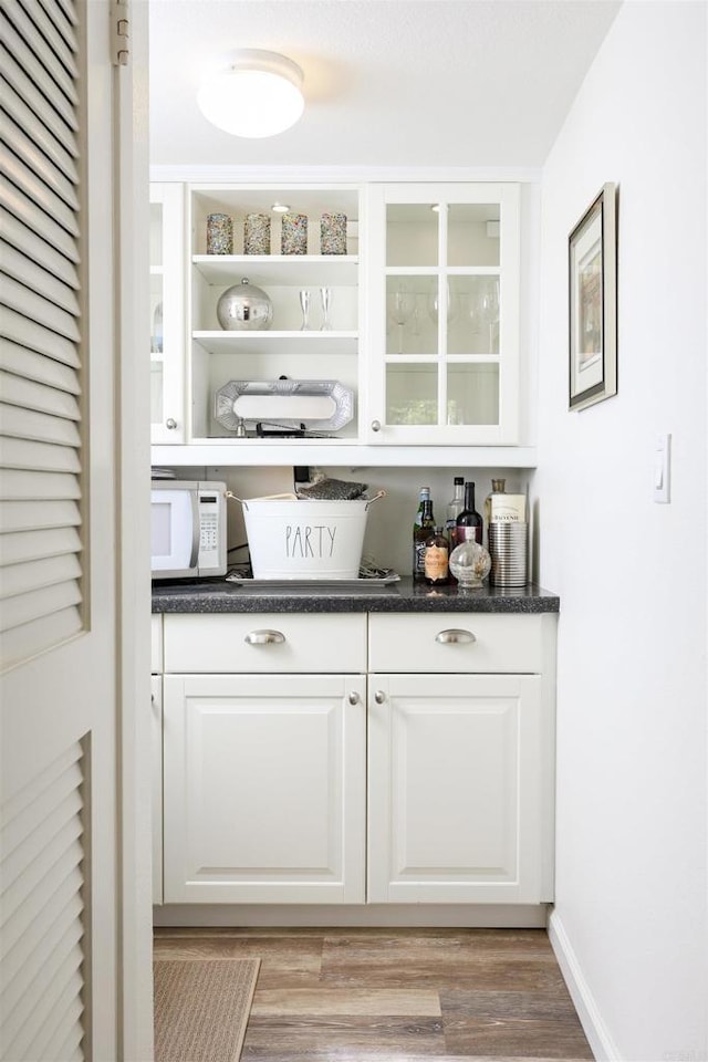 bar featuring white microwave, baseboards, and light wood-style floors