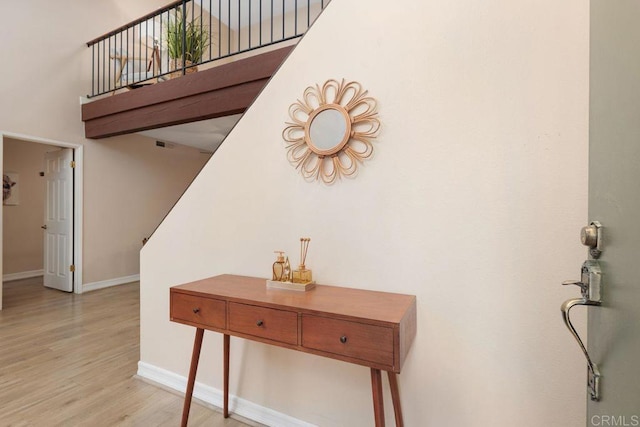 interior space with light wood-type flooring, baseboards, a high ceiling, and visible vents