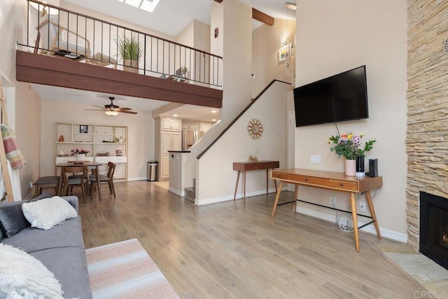 living area with a stone fireplace, light wood finished floors, baseboards, a towering ceiling, and stairs