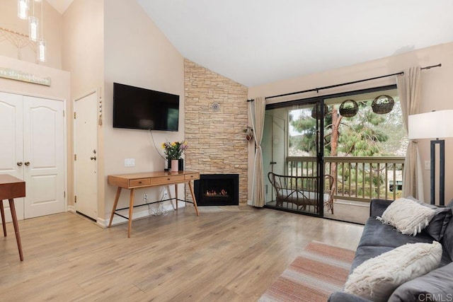 living room featuring high vaulted ceiling, a stone fireplace, and wood finished floors