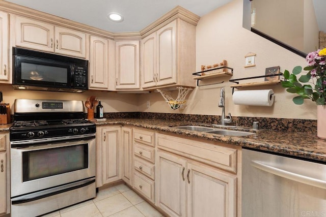 kitchen featuring dark stone countertops, appliances with stainless steel finishes, cream cabinets, light tile patterned flooring, and a sink