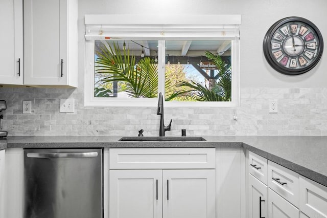 kitchen featuring dark countertops, backsplash, dishwasher, white cabinets, and a sink