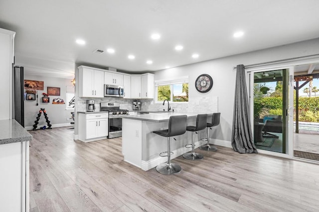 kitchen featuring light wood-style flooring, a sink, backsplash, appliances with stainless steel finishes, and a peninsula