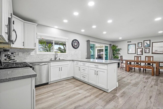 kitchen with light wood-type flooring, a sink, tasteful backsplash, a peninsula, and dishwasher