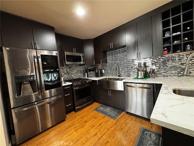 kitchen with a sink, light wood-type flooring, tasteful backsplash, and appliances with stainless steel finishes