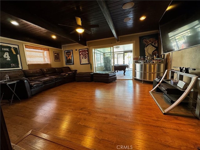 living area featuring beamed ceiling, wooden ceiling, a ceiling fan, and wood finished floors