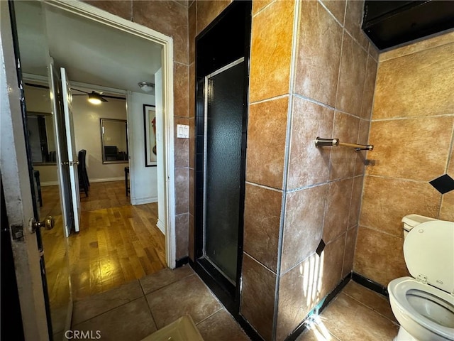 full bath with a shower stall, toilet, tile walls, and tile patterned floors