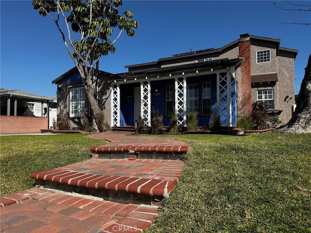 view of front of house with a front yard, a porch, a chimney, and stucco siding