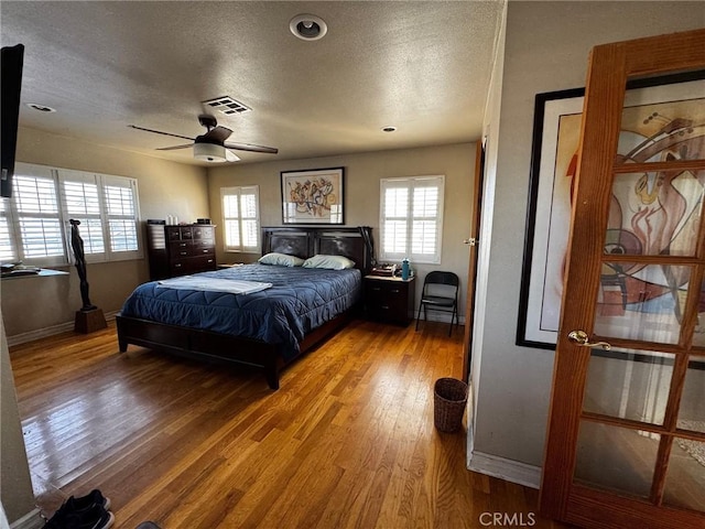 bedroom with baseboards, wood finished floors, visible vents, and a textured ceiling