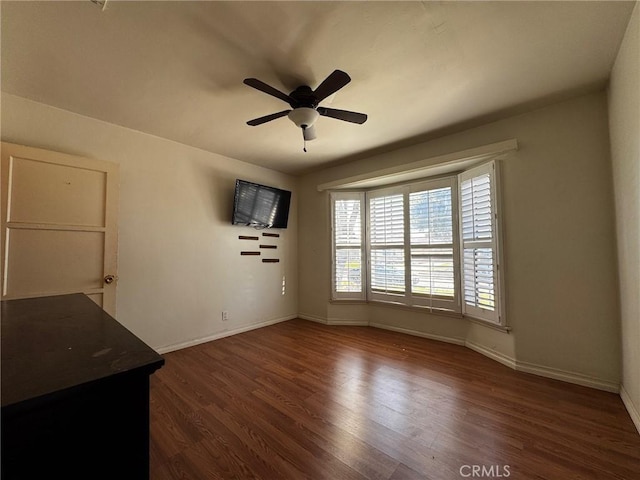 unfurnished living room featuring dark wood-style floors, baseboards, and a ceiling fan