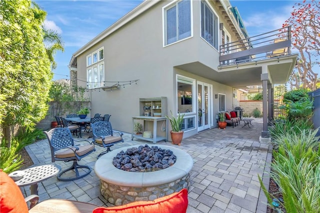 rear view of property featuring stucco siding, a patio, fence, french doors, and a balcony