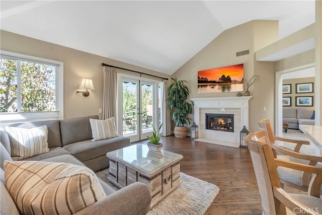 living room with a tiled fireplace, vaulted ceiling, wood finished floors, and visible vents