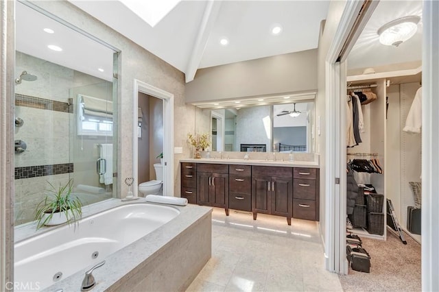 full bathroom featuring toilet, a stall shower, vaulted ceiling with skylight, a tub with jets, and vanity