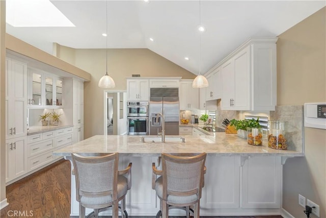 kitchen with appliances with stainless steel finishes, white cabinetry, a peninsula, and vaulted ceiling