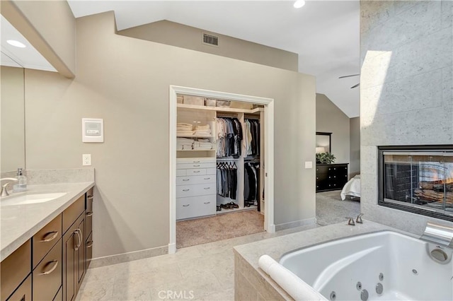 full bathroom with a multi sided fireplace, a tub with jets, vanity, and vaulted ceiling