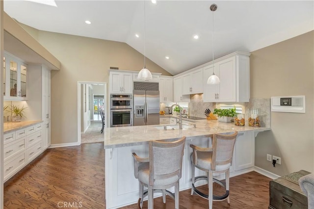 kitchen with lofted ceiling, a peninsula, a sink, appliances with stainless steel finishes, and white cabinetry