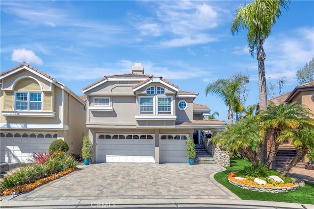 view of front of home featuring stairs, stucco siding, a chimney, decorative driveway, and a garage