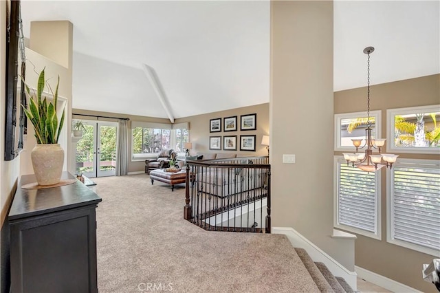 interior space featuring baseboards, carpet, an upstairs landing, a notable chandelier, and high vaulted ceiling