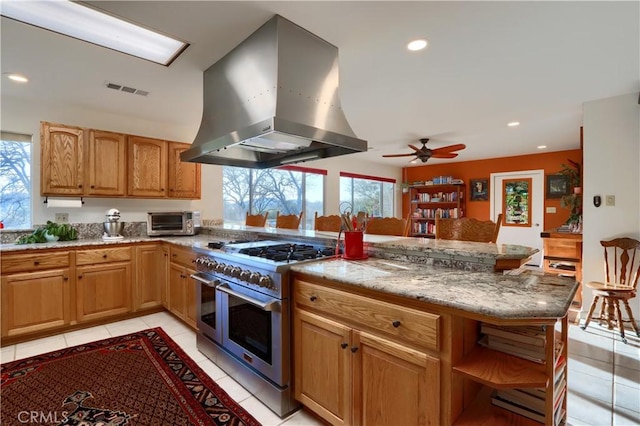 kitchen featuring light tile patterned floors, double oven range, a peninsula, and island range hood