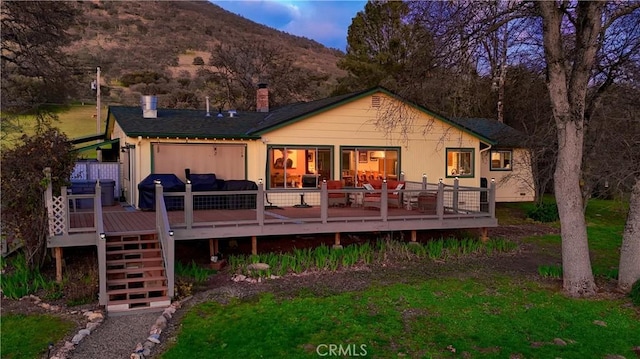 rear view of property with stairway, a lawn, a deck with mountain view, and a chimney