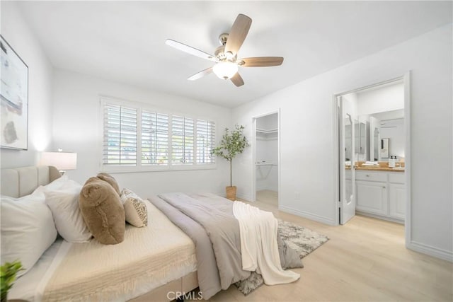 bedroom with a walk in closet, ceiling fan, baseboards, ensuite bathroom, and light wood-style floors