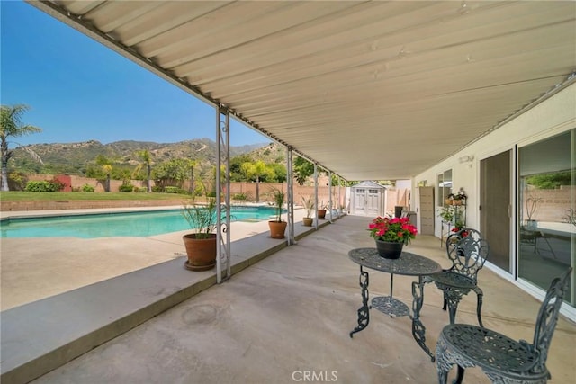 view of swimming pool featuring a storage unit, a fenced backyard, a mountain view, an outdoor structure, and a patio area