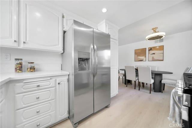 kitchen with visible vents, light wood-style flooring, stainless steel fridge with ice dispenser, light countertops, and white cabinets