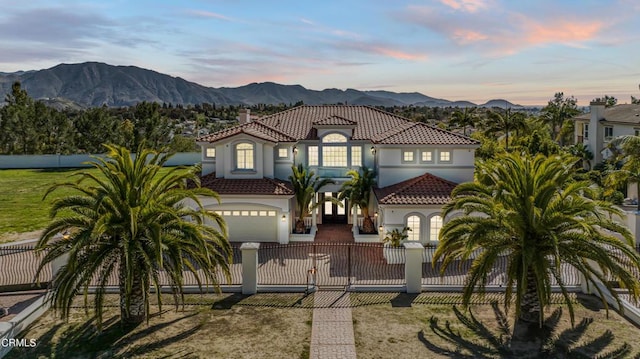 mediterranean / spanish home with stucco siding, a garage, a fenced front yard, a tiled roof, and a mountain view