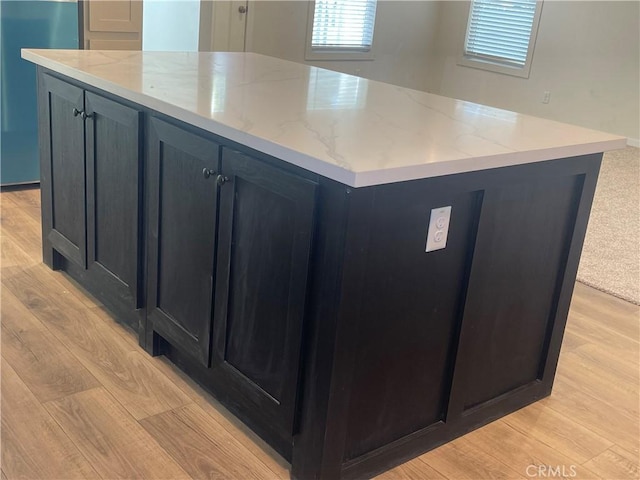 kitchen with light stone countertops, a center island, and light wood finished floors