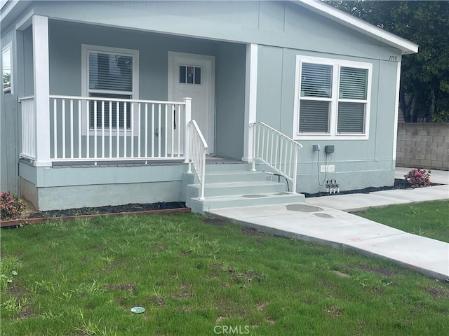 view of exterior entry featuring covered porch and a lawn