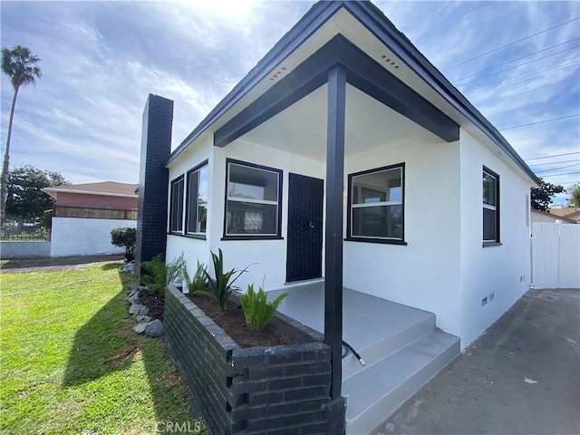 view of front of home with a front yard, fence, a chimney, stucco siding, and crawl space