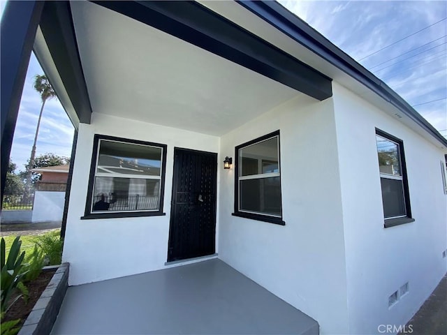 view of exterior entry with crawl space, stucco siding, and visible vents