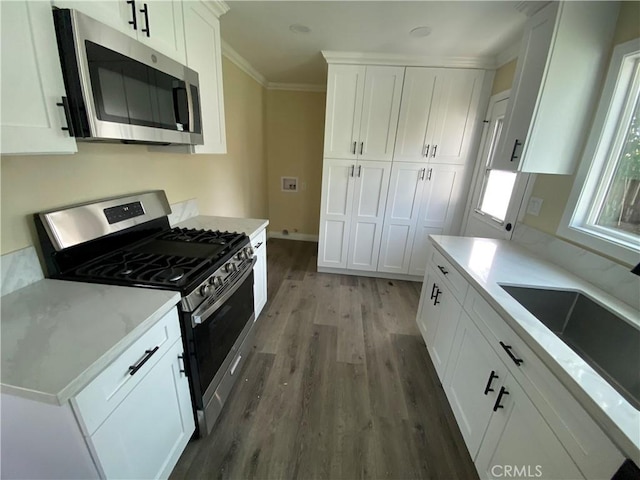 kitchen featuring crown molding, stainless steel appliances, wood finished floors, white cabinetry, and a sink