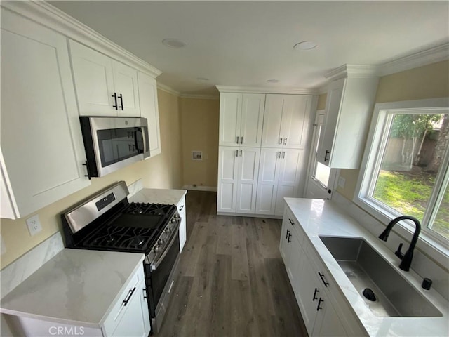 kitchen with wood finished floors, a sink, white cabinets, appliances with stainless steel finishes, and crown molding