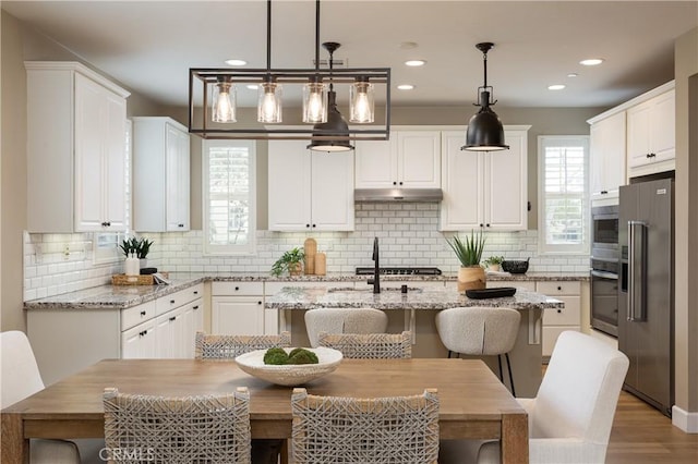 kitchen with backsplash, appliances with stainless steel finishes, a kitchen island with sink, and white cabinetry