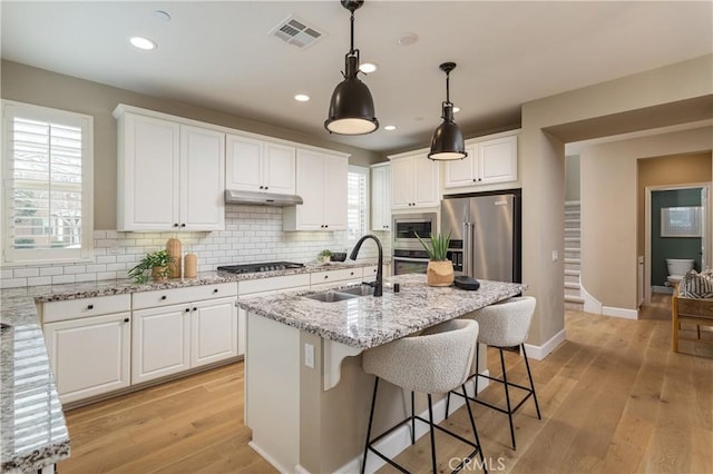 kitchen with visible vents, under cabinet range hood, appliances with stainless steel finishes, light wood-style floors, and a sink