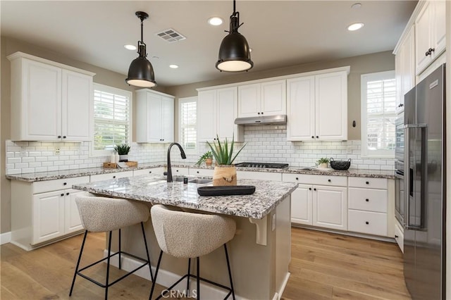 kitchen with visible vents, light wood-style flooring, a sink, under cabinet range hood, and built in fridge