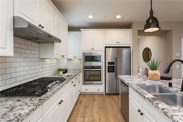 kitchen with under cabinet range hood, light wood-style flooring, appliances with stainless steel finishes, white cabinetry, and a sink