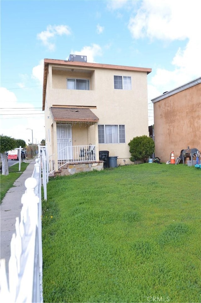 rear view of house with fence, a porch, stucco siding, a lawn, and a balcony