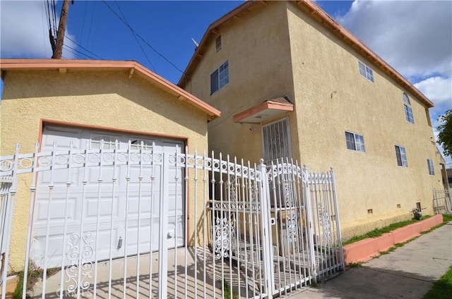 view of property exterior featuring stucco siding, a gate, fence, an attached garage, and crawl space