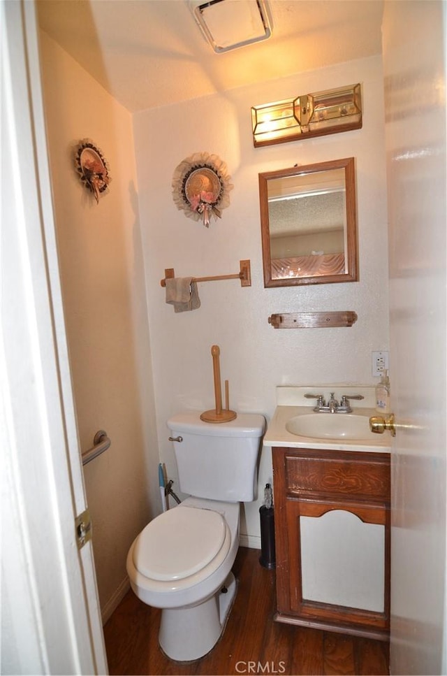 half bath with visible vents, toilet, wood finished floors, baseboards, and vanity